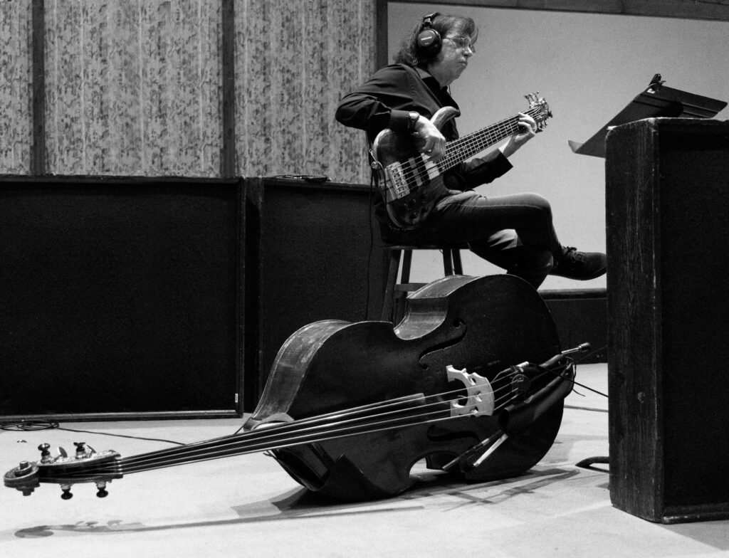 Black and white photo of Phil Ravita recording on electric bass with an upright bass resting nearby